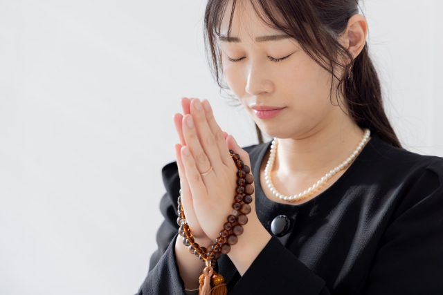 手を合わせる喪服の女性